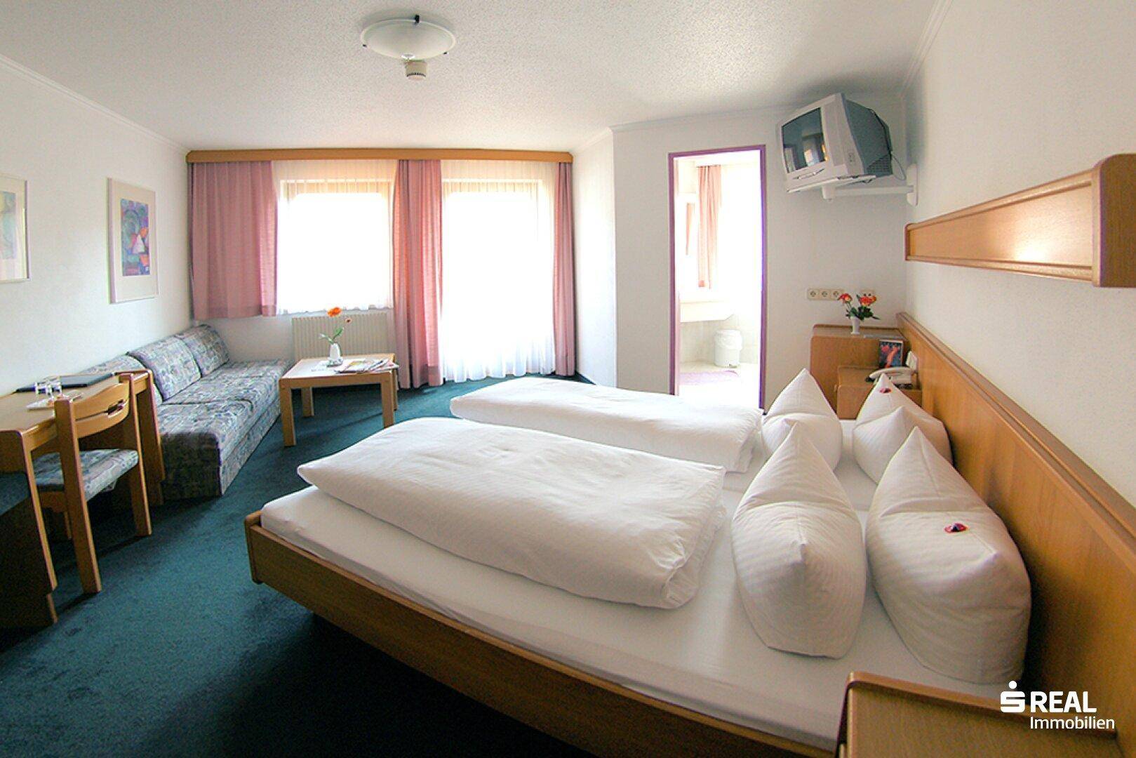 Helles Schlafzimmer mit zwei Einzelbetten, Sofa, Schreibtisch und Teppichboden.