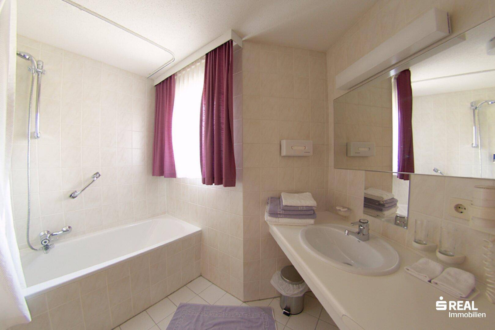 Funktionales Badezimmer mit Badewanne, Waschbecken, Spiegel und Fenster.