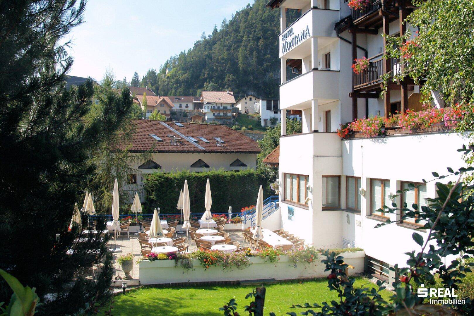 Sonniger Außenbereich mit Tischen, Sonnenschirmen und Blick auf die umliegende Landschaft und Berge.