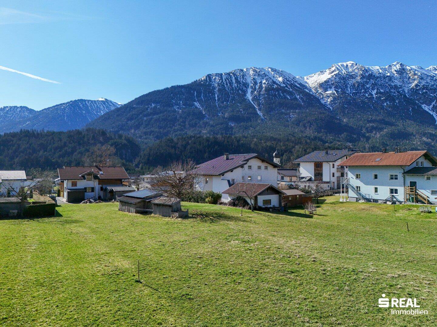 Malerisches Dorf mit traditionellen Häusern und Kirchturm, eingebettet in eine grüne Landschaft vor schneebedeckten Bergen.