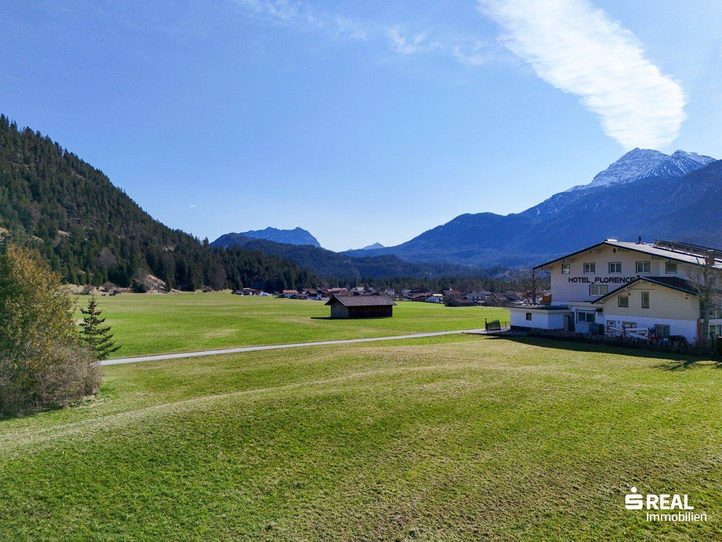 Hotelgebäude "Florence" inmitten einer grünen Wiese, umgeben von schneebedeckten Bergen unter strahlend blauem Himmel.