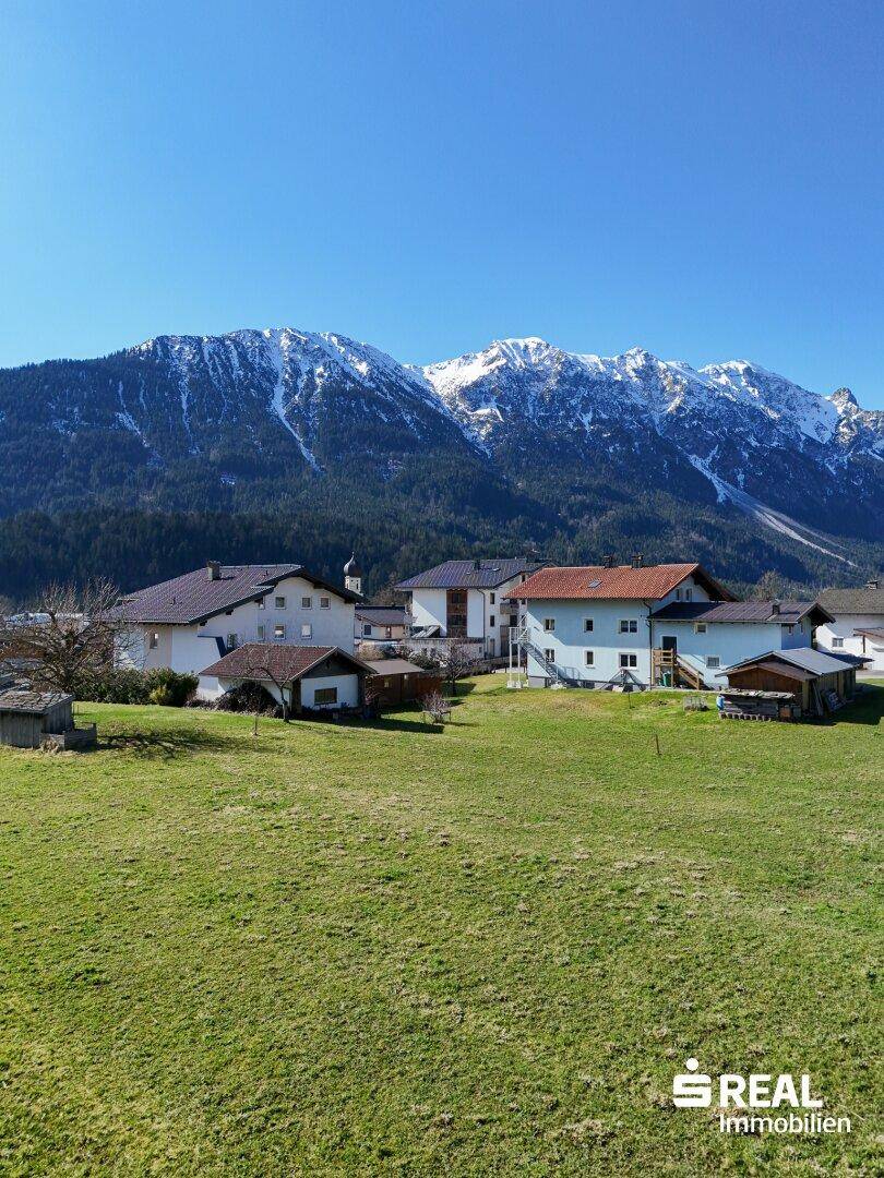 Malerisches Dorf mit traditionellen Häusern und Kirchturm, eingebettet in eine grüne Landschaft vor schneebedeckten Bergen.