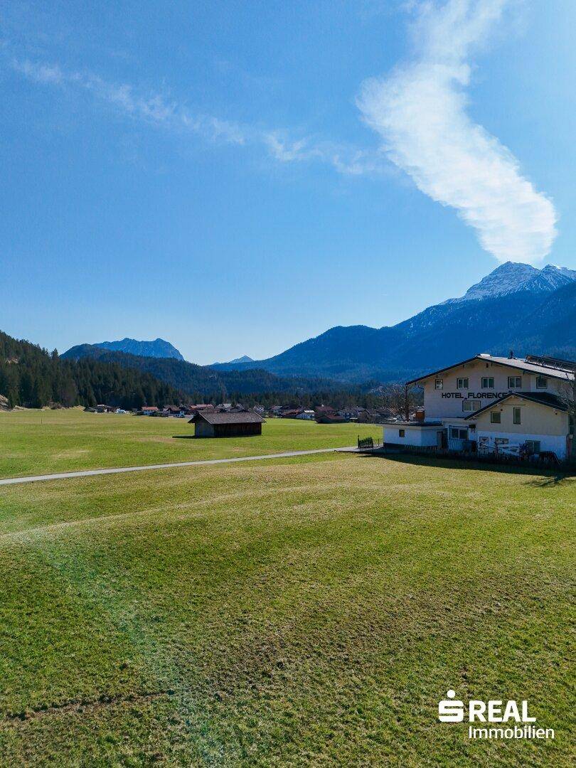 Hotelgebäude "Florence" inmitten einer grünen Wiese, umgeben von schneebedeckten Bergen unter strahlend blauem Himmel.