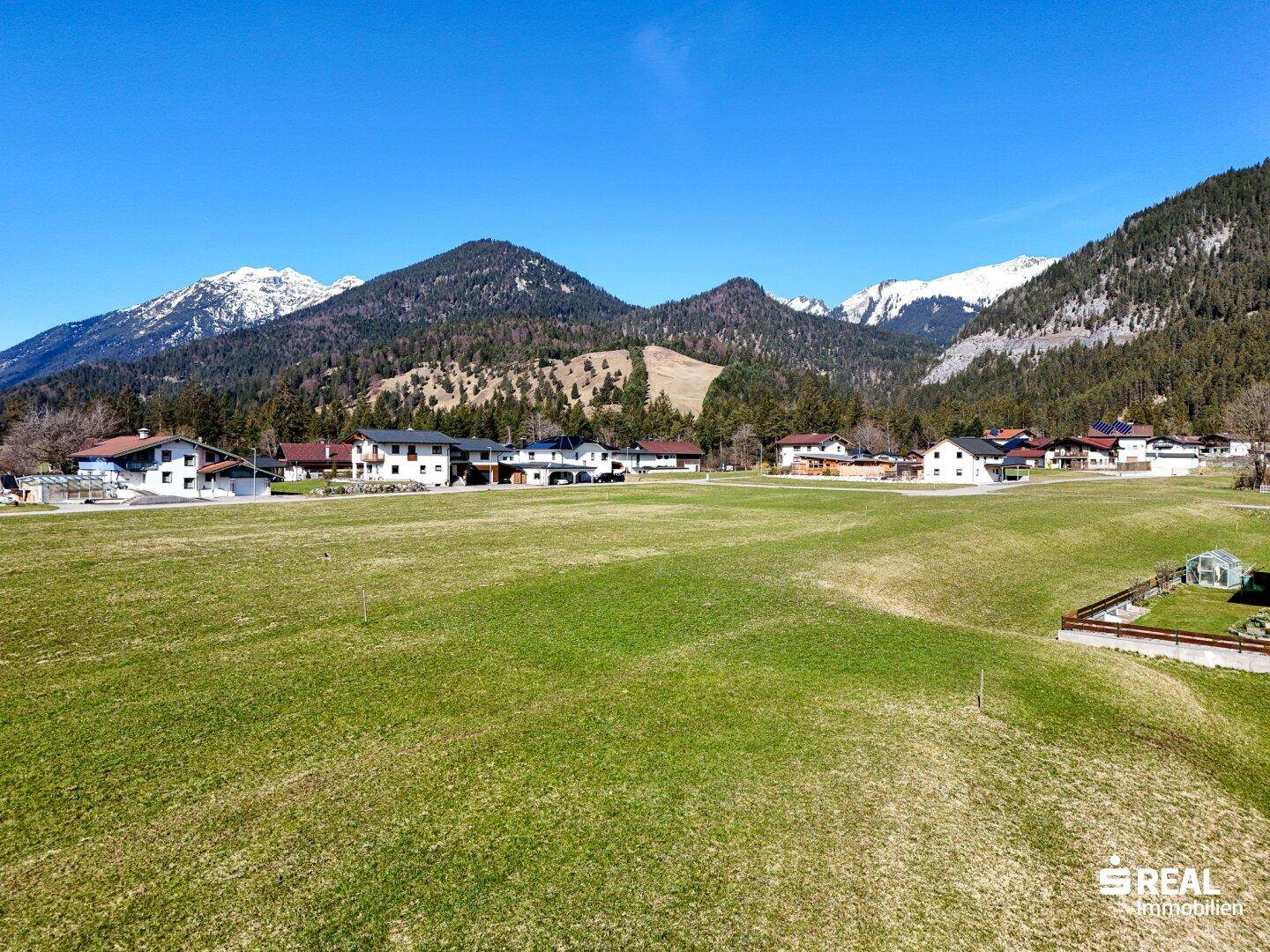 Panoramablick auf die umliegende Berglandschaft mit grünen Wiesen und Wohnhäusern.