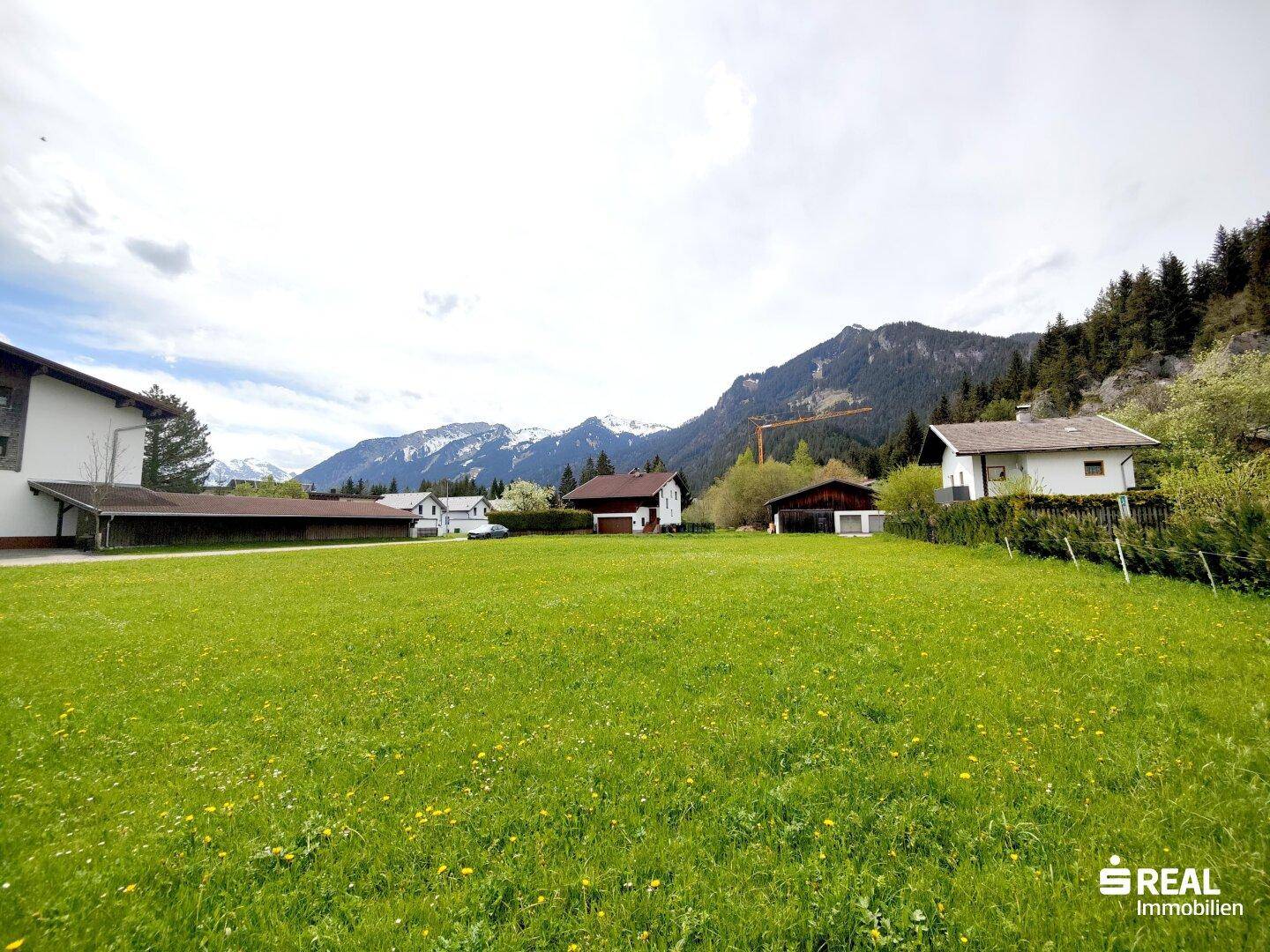 Weitläufige Grünfläche mit Blick auf die umliegende Berglandschaft und vereinzelte Häuser.