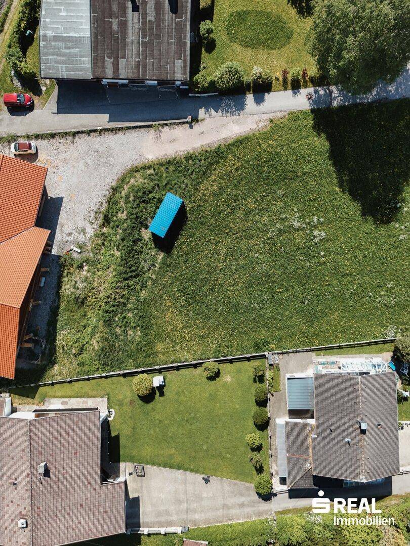 Vogelperspektive eines unbebauten Grundstücks mit angrenzenden Gärten und Gebäuden in ländlicher Umgebung.