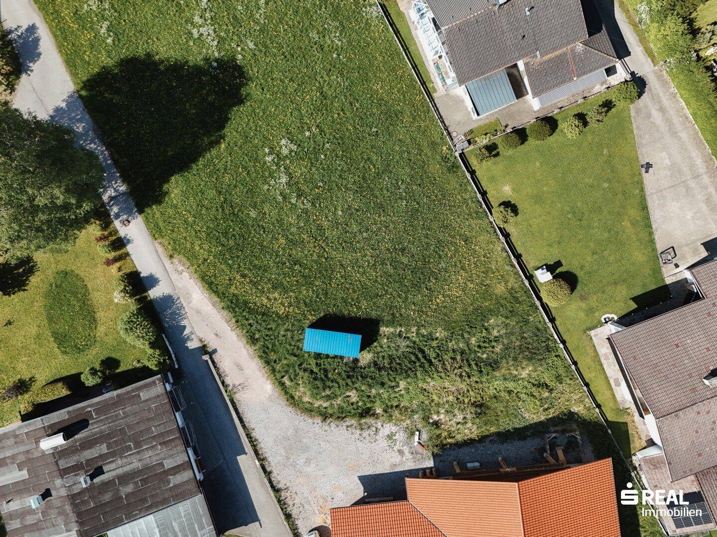Luftbild eines unbebauten Grundstücks mit angrenzenden Gebäuden und einer Zufahrtsstraße.