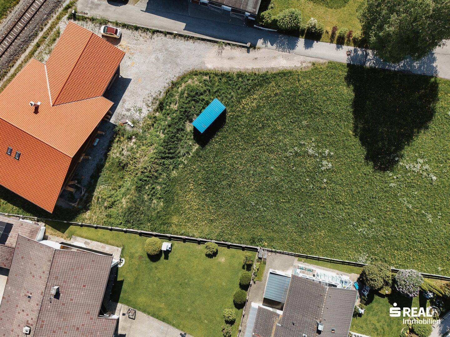 Drohnenaufnahme eines Baugrundstücks mit blauer Markierung, umgeben von Wohnbebauung und Grünflächen.