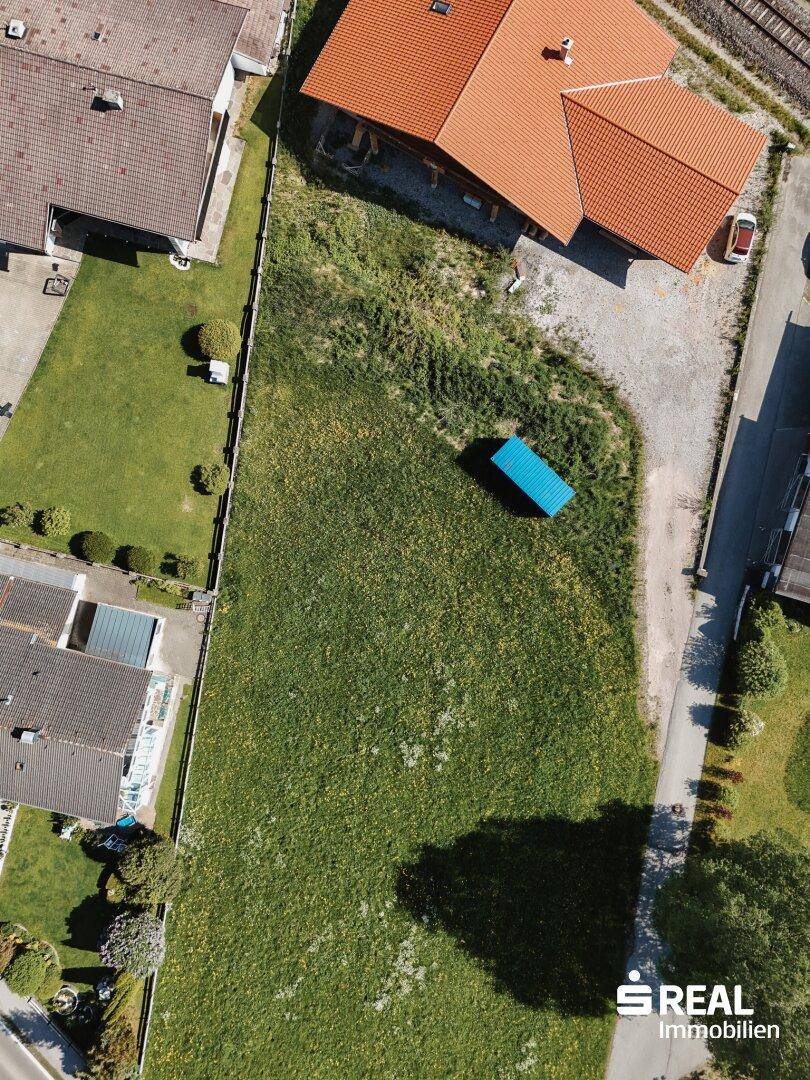 Luftaufnahme eines potenziellen Baugrundstücks mit blauer Umrandung, eingebettet in eine Wohnsiedlung.