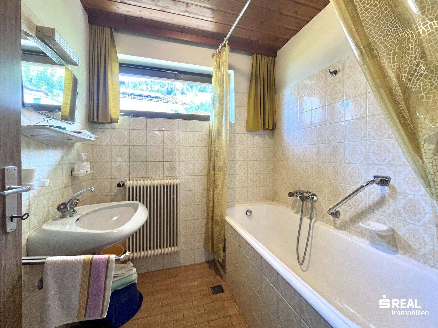 Badezimmer im 80er-Jahre-Stil mit Badewanne, Waschbecken und Fenster.
