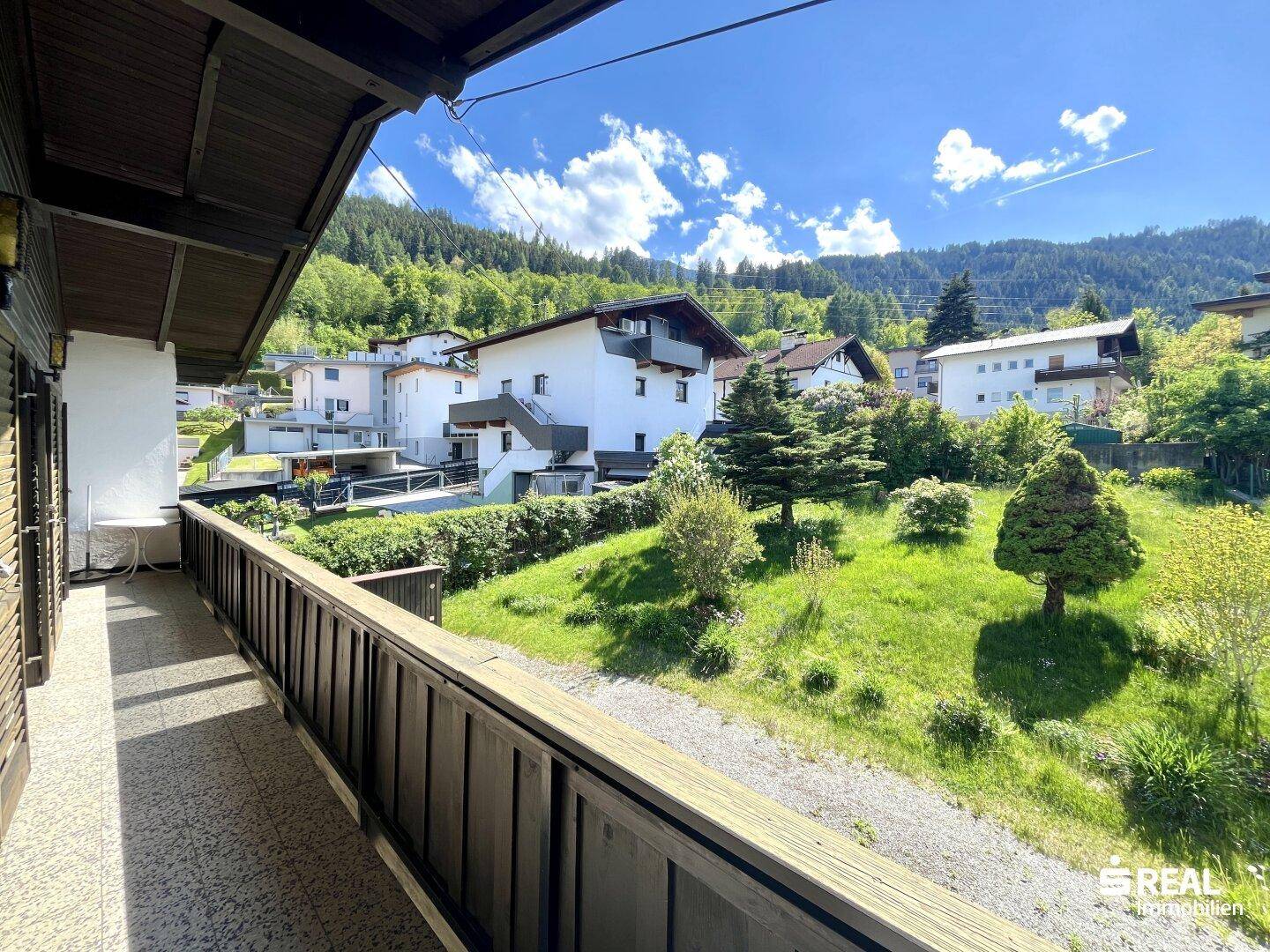Langer Balkon mit Holzboden und Blick auf die grüne Hügellandschaft.