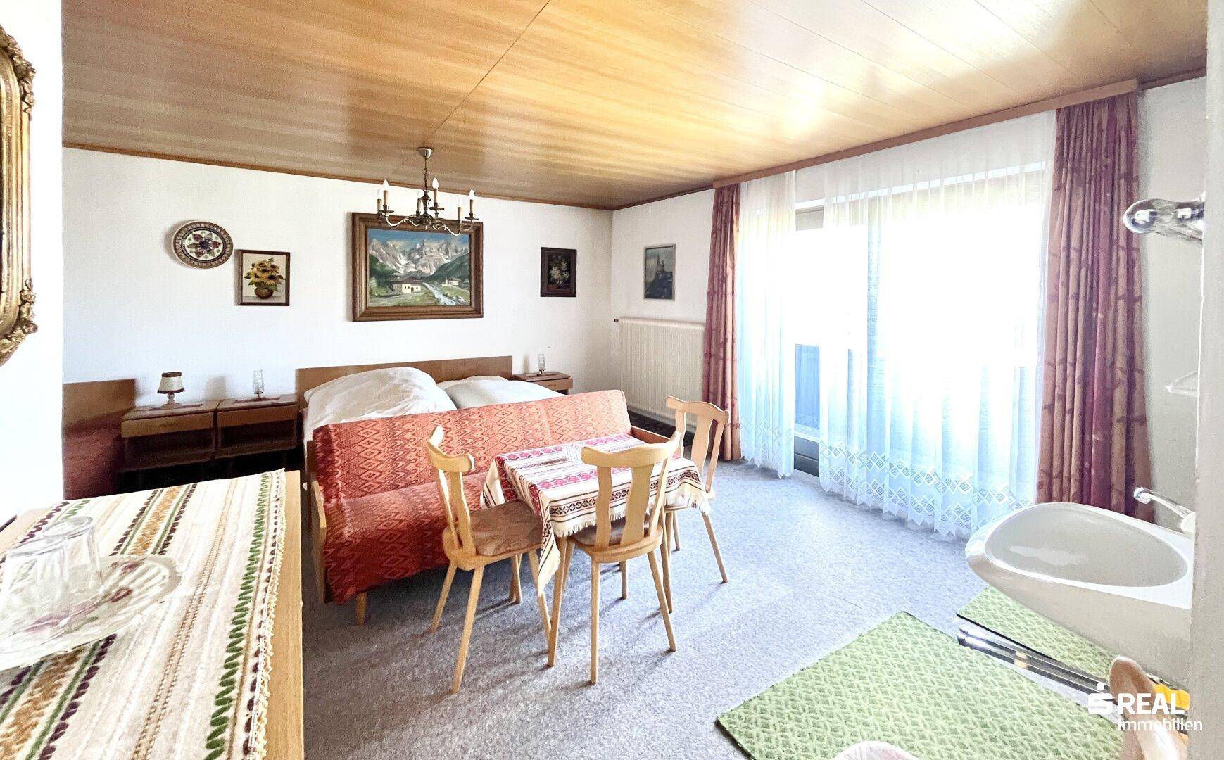Helles Schlafzimmer mit Doppelbett, kleinem Essbereich und integriertem Waschbecken.