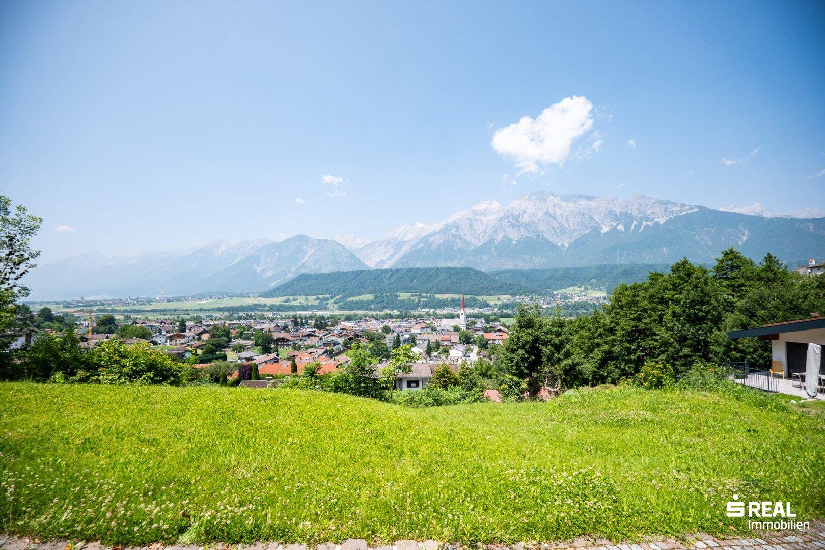 Panoramablick über eine malerische Stadt mit majestätischen Bergen im Hintergrund unter blauem Himmel.