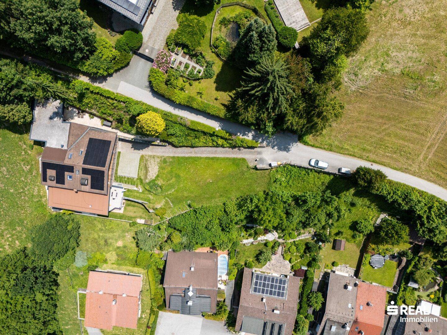 Weitläufige Luftaufnahme einer Wohnsiedlung mit Einfamilienhäusern, Gärten und einer Zufahrtsstraße.