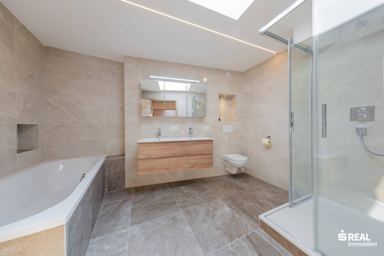 Modernes Badezimmer mit Badewanne, Dusche, Doppelwaschbecken und Oberlicht für natürliches Licht.