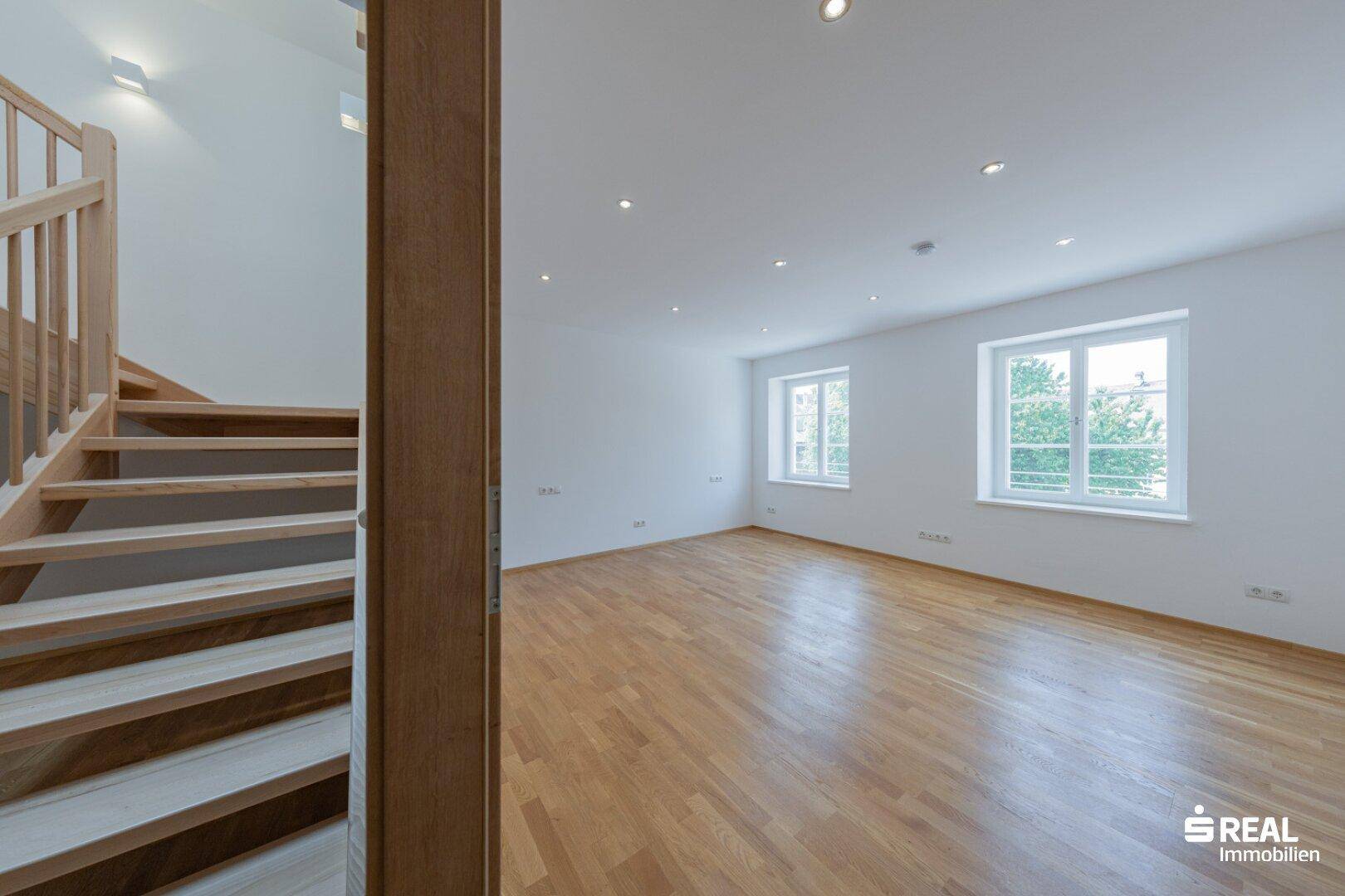 Geräumiges Wohnzimmer mit hellem Parkettboden und Holztreppe, die in die obere Etage führt.