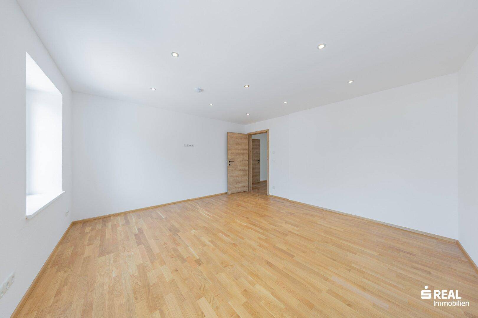 Heller Raum mit Parkettboden und weiß gestrichenen Wänden, ideal als Schlaf- oder Wohnzimmer.