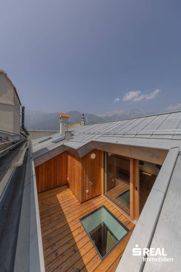 Dachterrasse mit Holzbelag und Blick auf die Berge und die umliegende Stadt.
