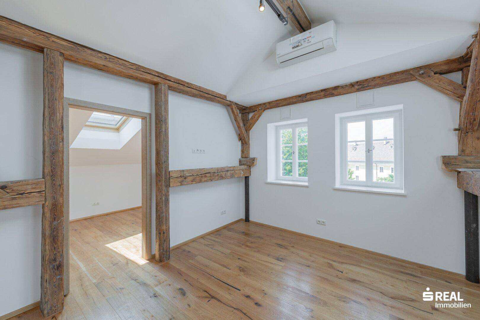 Helles Zimmer im Dachgeschoss mit Holzbalken, Parkettboden und Klimaanlage.