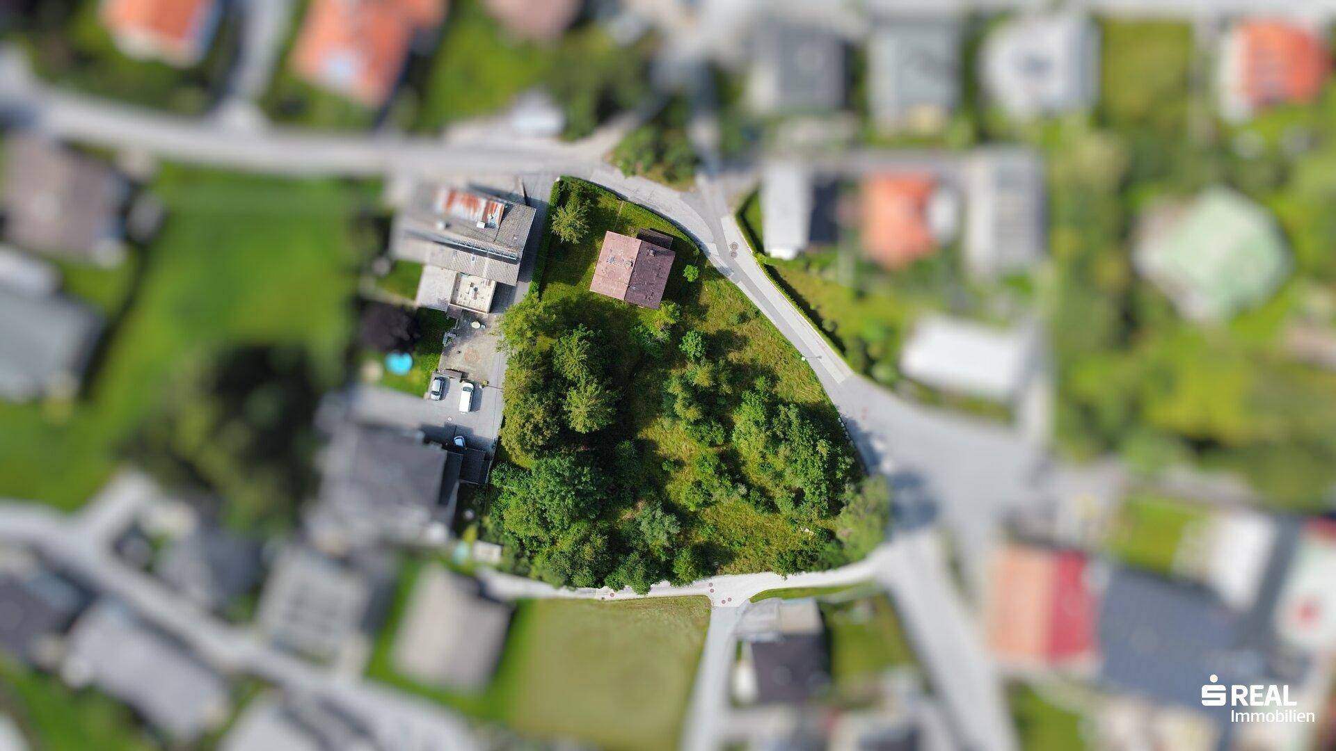 Weitläufige Luftaufnahme eines Wohngebiets mit einem zentralen, grünen Grundstück und umliegenden Häusern.