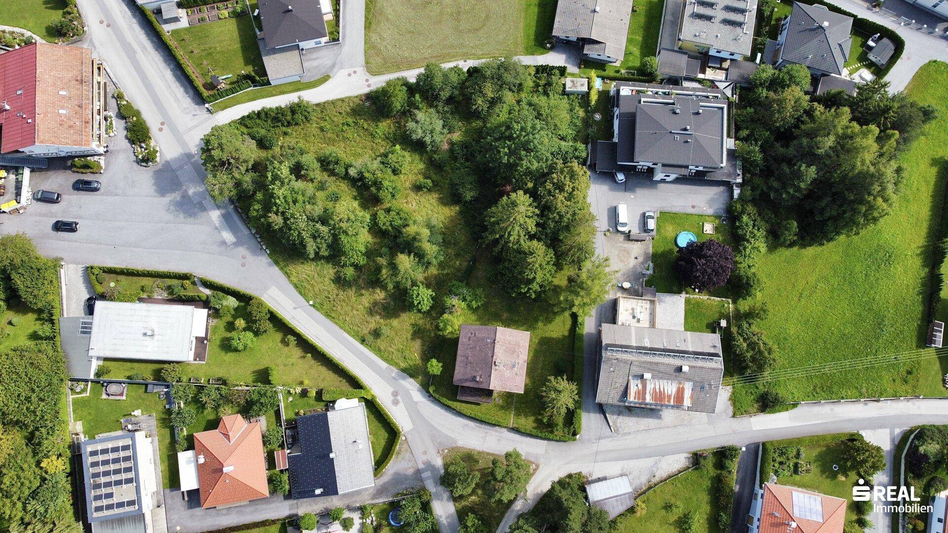 Luftbild eines Wohngebiets mit einem großen, grünen Grundstück und angrenzenden Straßen und Gebäuden.