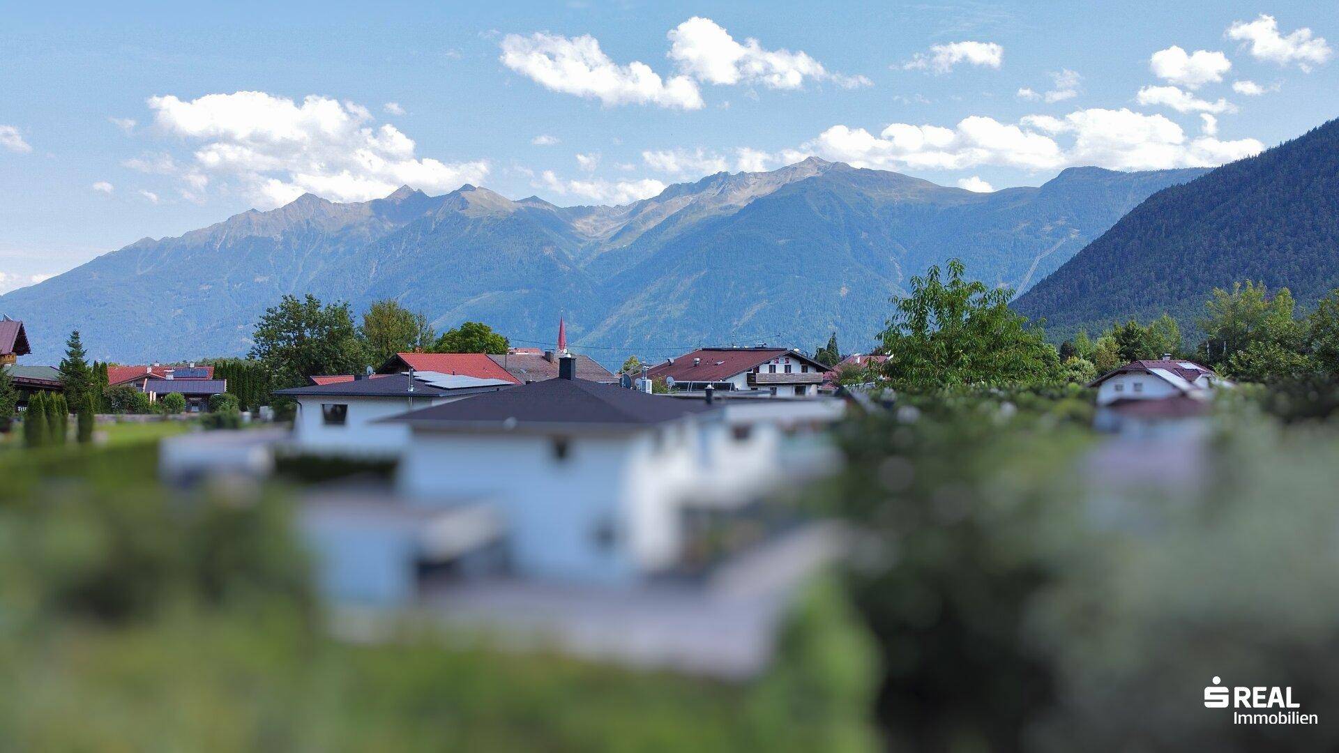 Blick auf eine Wohnsiedlung mit traditionellen Häusern vor einer beeindruckenden Bergkulisse unter blauem Himmel.