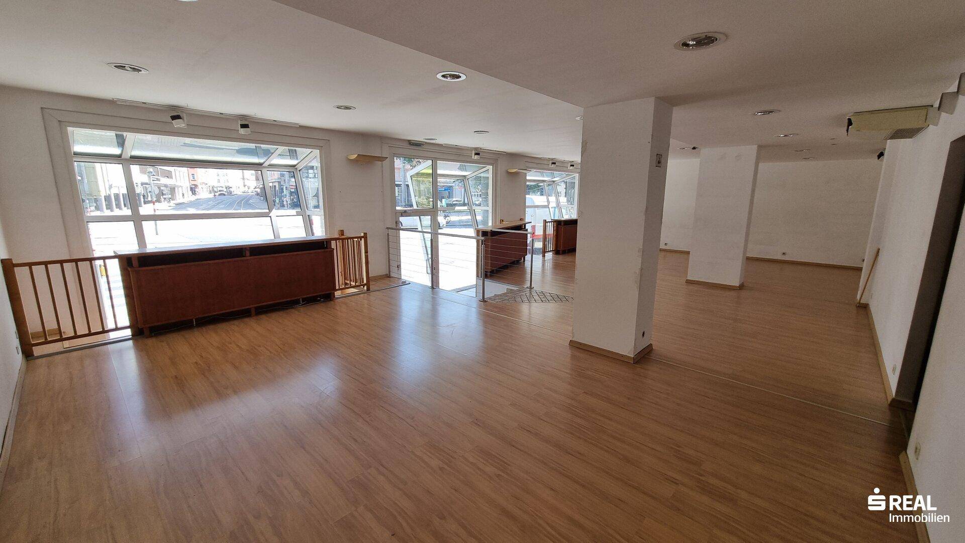 Weitläufiger Innenbereich mit Laminatboden, großen Schaufenstern und Blick auf die Stadtstraße.