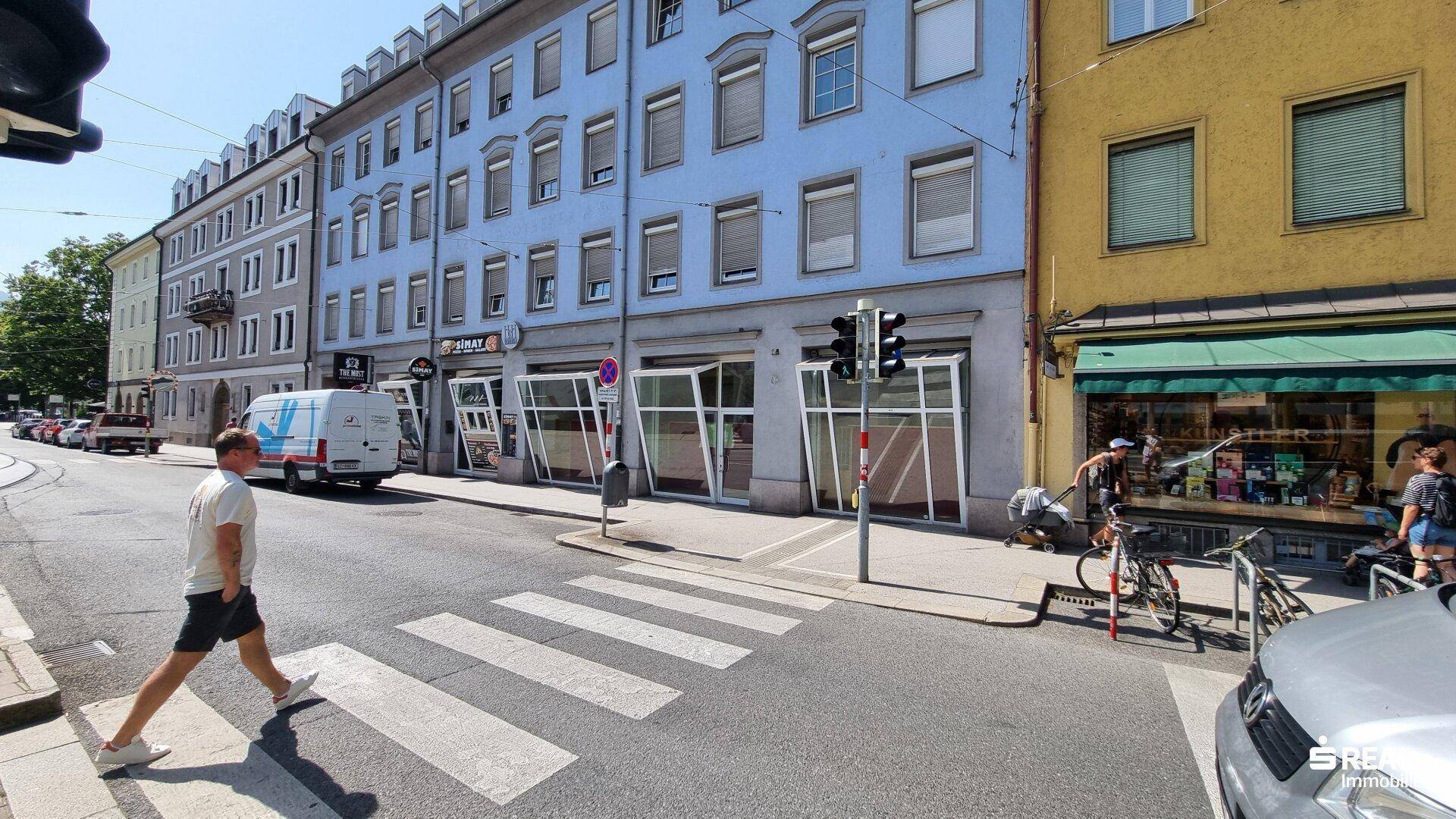 Gebäudefassade mit großen Schaufenstern im Erdgeschoss und darüberliegenden Wohnungen in der Stadt.