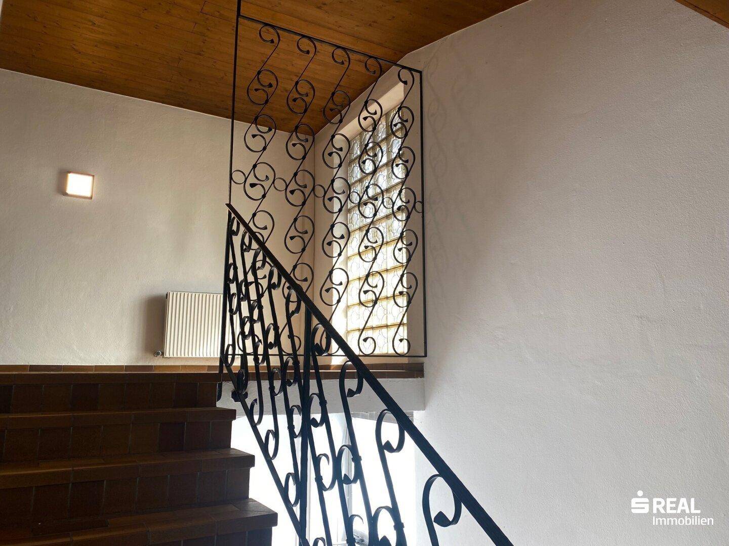 Treppenhaus mit kunstvollem schmiedeeisernem Geländer und Holzdecke, die zum Obergeschoss führt.