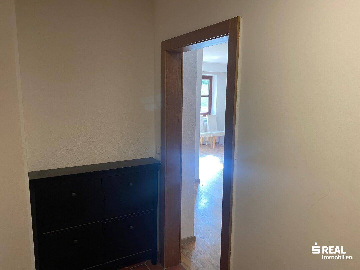 Schmaler Flur mit dunklem Schuhschrank und Blick in einen hellen Nebenraum.