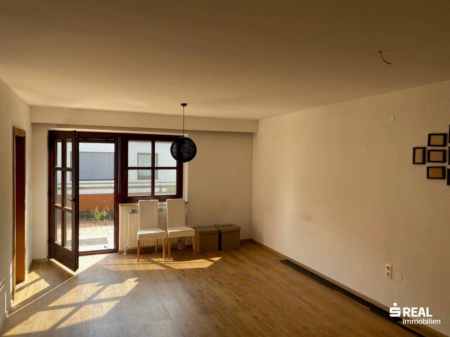 Helles Wohnzimmer mit Holzboden und Zugang zu einem Außenbereich, ideal für entspannte Stunden.