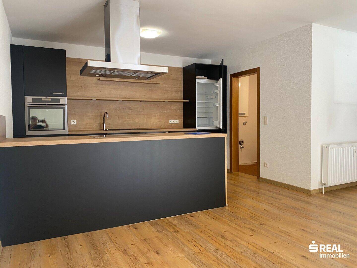 Funktionale Küche mit schwarzer Küchenzeile, Holzakzenten und integriertem Kühlschrank.