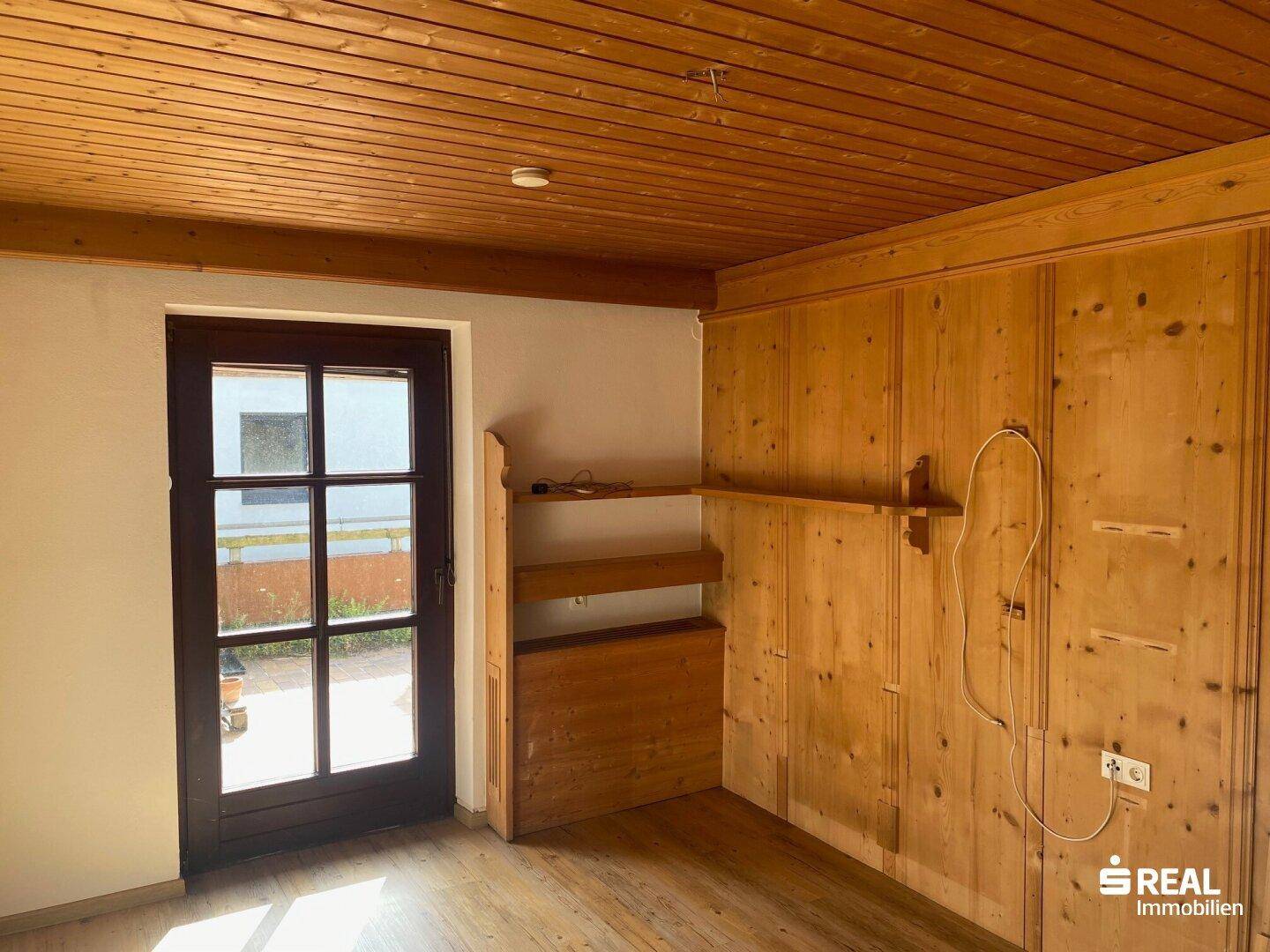 Rustikaler Raum mit Holzvertäfelung an Wänden und Decke sowie Zugang zum Außenbereich.