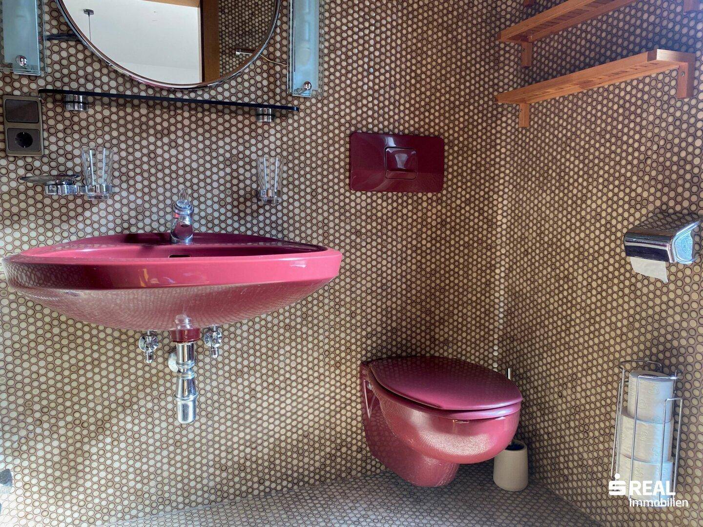 Gäste-WC mit auffälligen Mosaikfliesen, rotem Waschbecken und passender Wandtoilette.