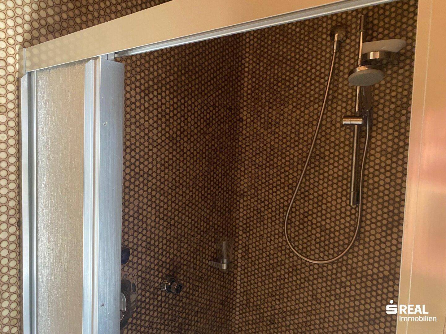Duschbereich mit braunen Mosaikfliesen und moderner Duscharmatur, gut gepflegt.