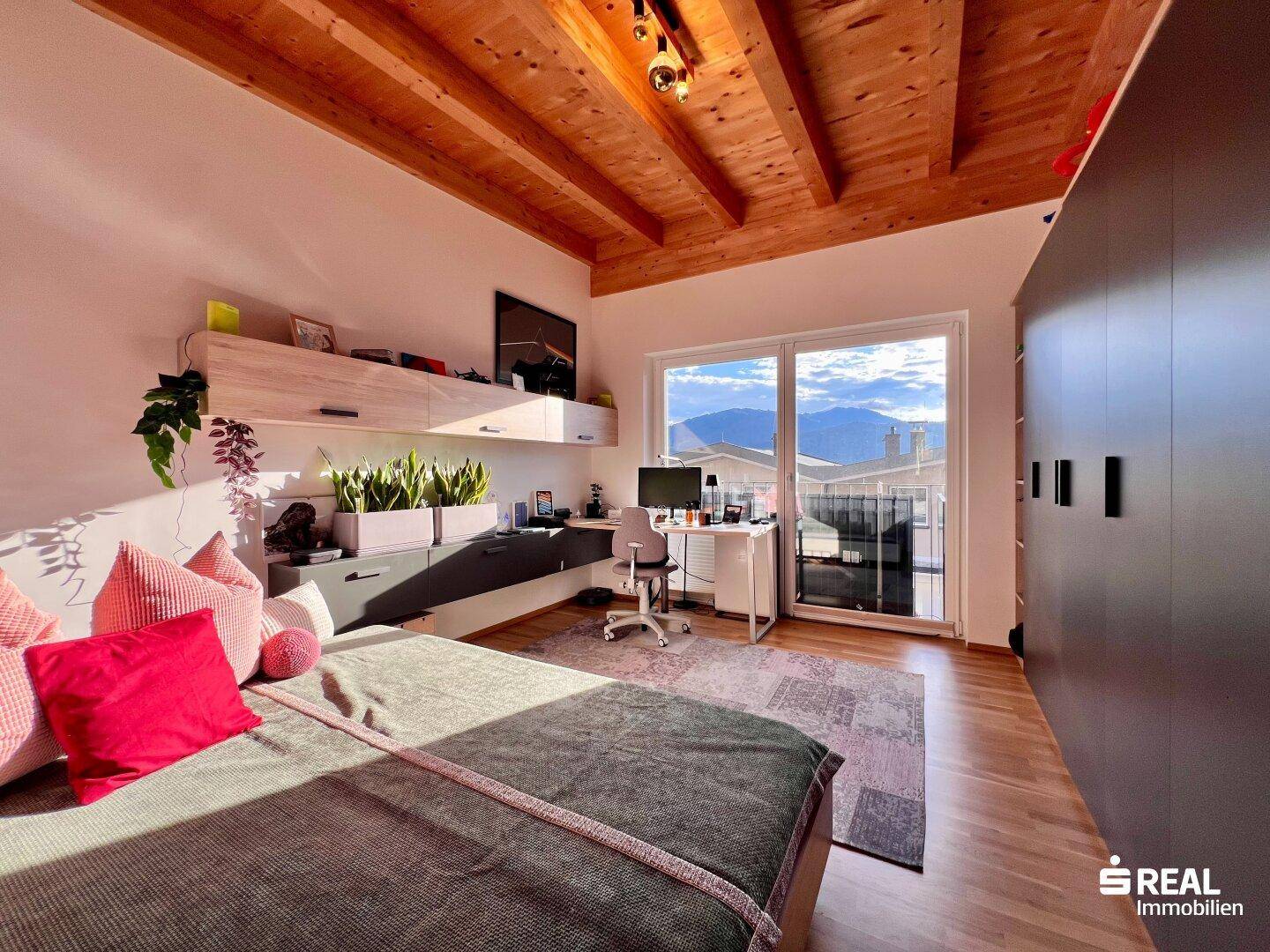 Geräumiges Schlafzimmer mit Holzbalkendecke, Schreibtisch und Balkonzugang mit Bergblick.