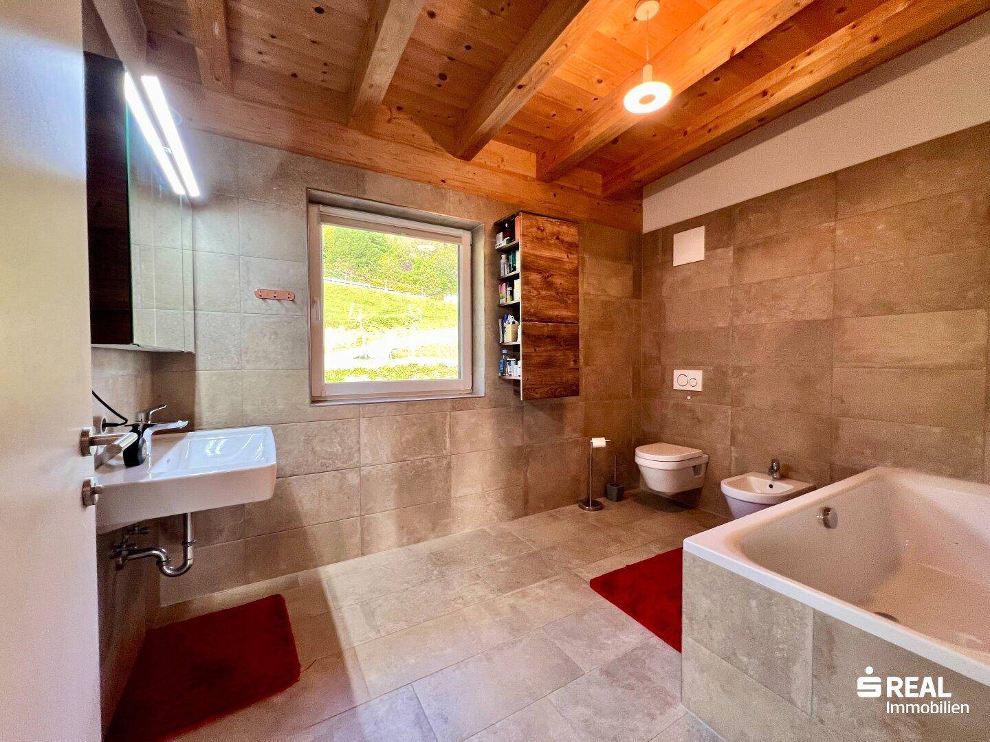 Großes Badezimmer mit Badewanne, Bidet, Fenster und Holzbalkendecke.