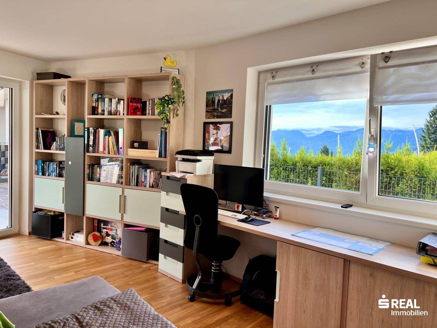 Arbeitsbereich mit großem Schreibtisch, Bücherregal und Panoramablick auf die Berge.