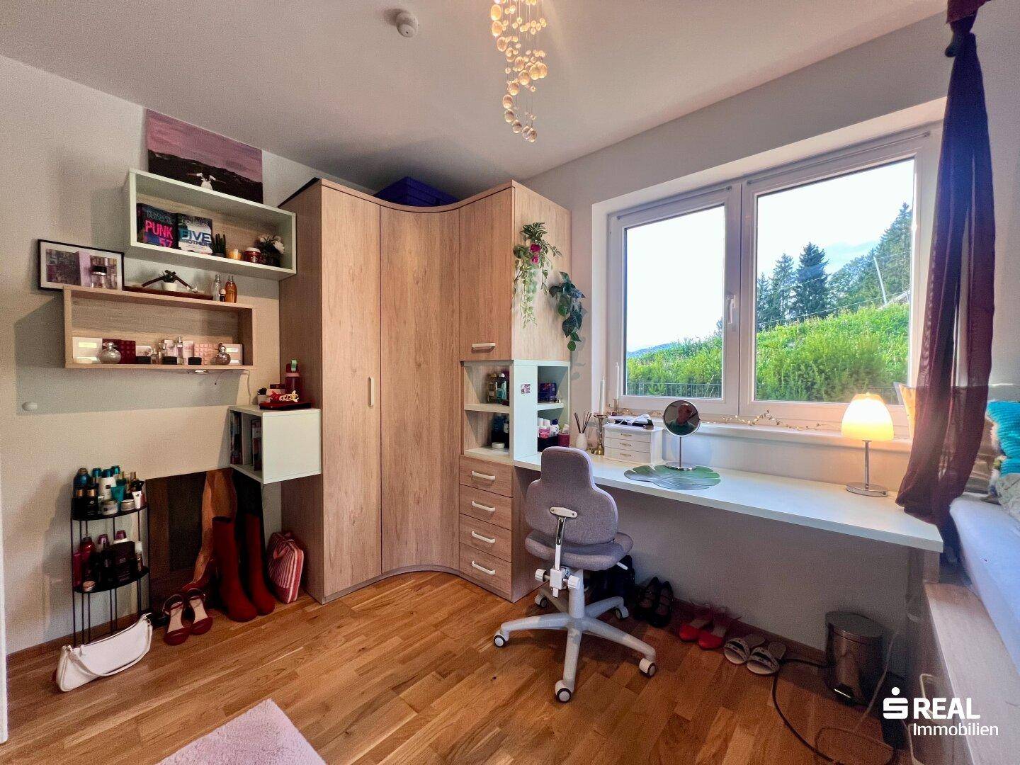 Kinderzimmer mit Schreibtisch am Fenster, Einbauschränken und Blick ins Grüne.