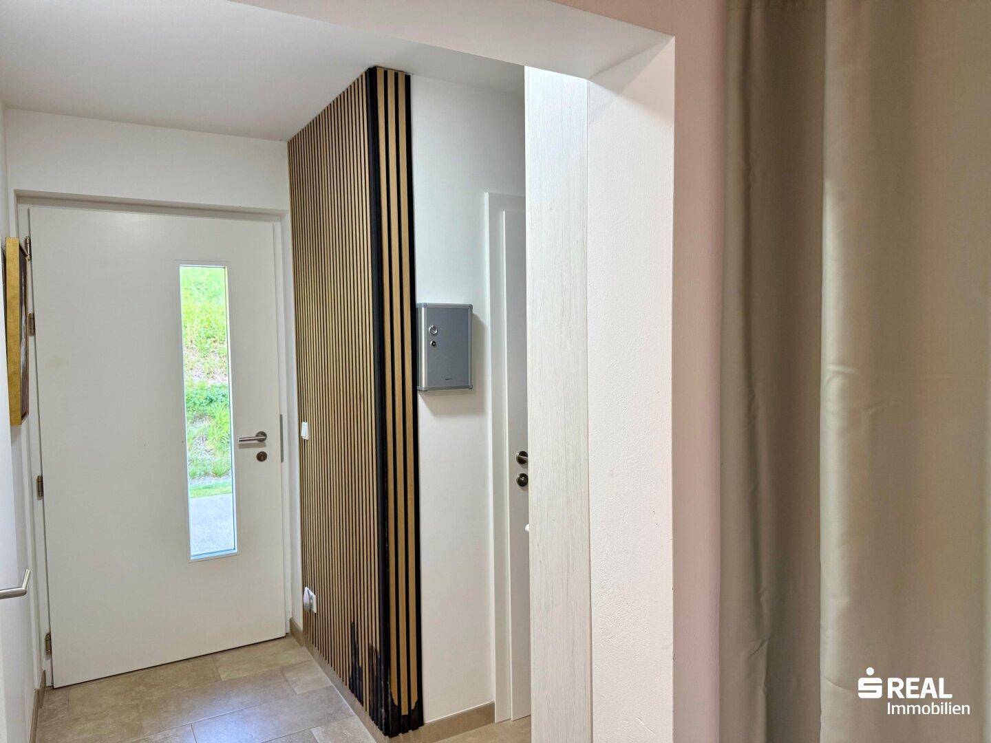 Heller Eingangsbereich mit moderner Holzlamellenwand und Fliesenboden.