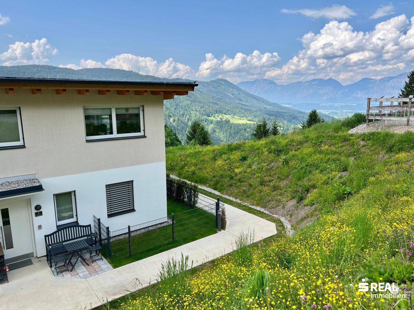 Außenansicht des Hauses mit blühender Wiese und weitem Blick auf die umliegende Berglandschaft.