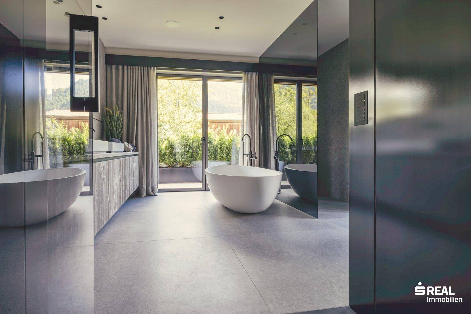 Luxuriöses Badezimmer mit zwei freistehenden Badewannen, großen Fenstern und Zugang zur Terrasse.