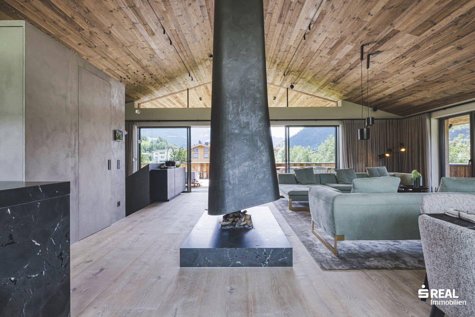 Offener Wohnbereich mit modernem Kamin, bequemen Sofas und Panoramablick auf die Berge.
