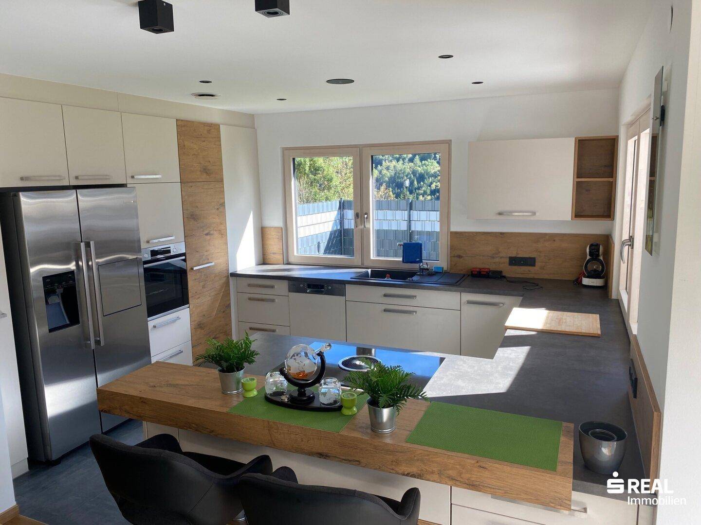 Moderne Einbauküche mit Kochinsel, Holzdetails und hochwertigen Geräten in hellem Design.