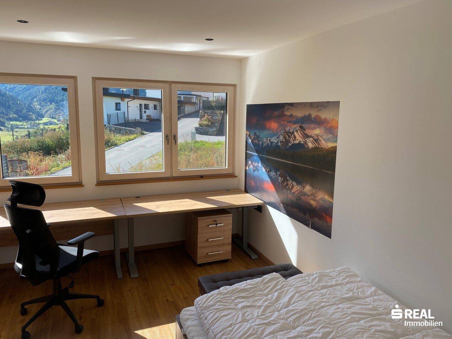 Helles Arbeitszimmer mit Holzboden, großem Schreibtisch und Blick auf die grüne Umgebung.