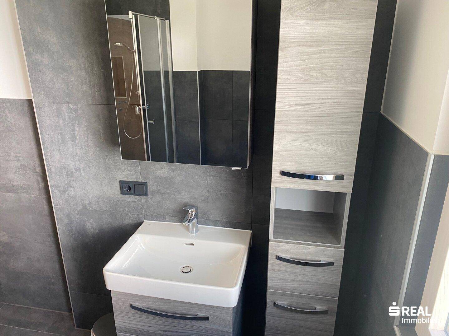 Modernes Badezimmer mit dunklen Fliesen, Waschtisch und Spiegelschrank, funktional und hell.