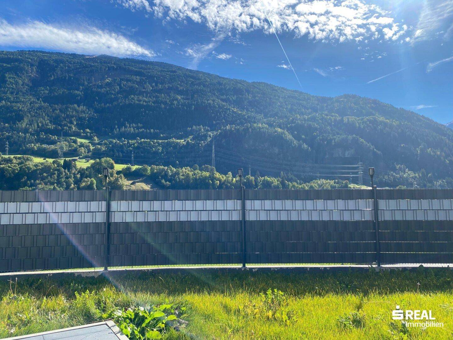 Weitläufiger Blick auf die umliegende Berglandschaft und grüne Natur unter blauem Himmel.