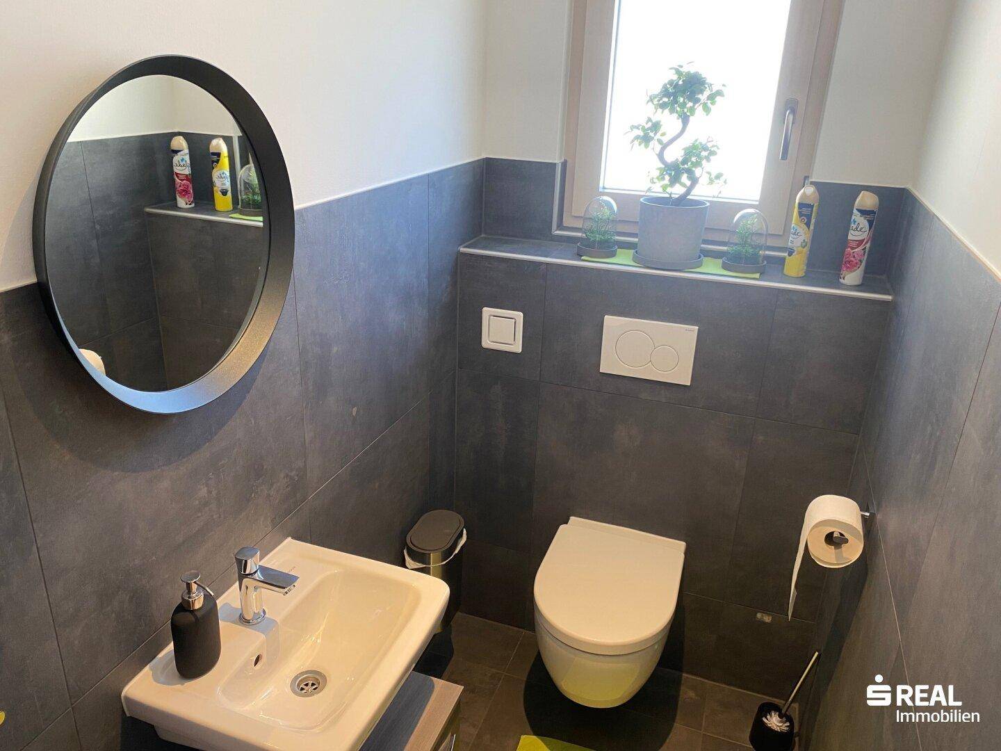 Modernes Gäste-WC mit dunklen Fliesen, wandhängendem WC und kleinem Fenster.