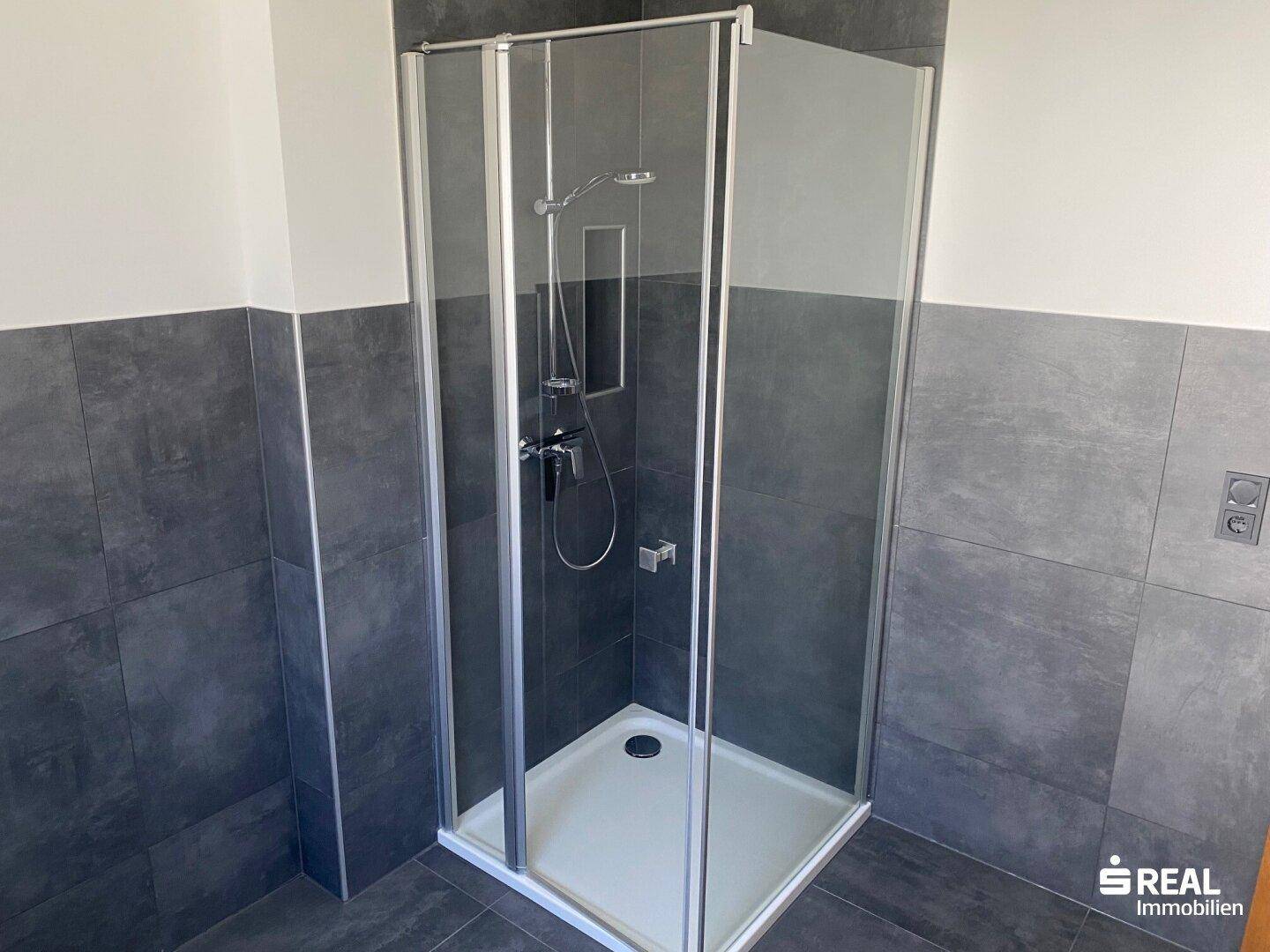 Modernes Badezimmer mit Duschkabine und dunklen Fliesen, funktional und sauber.