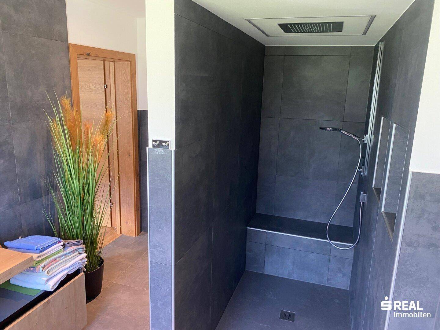 Geräumige, begehbare Dusche mit Regenduschkopf und Sitzbank, modern gefliest.